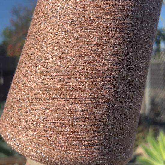 A luxurious cone of Pecci Filati SHIMMER yarn, a modern 50% Cotton, 25% Linen, 14% Polyester, and 12% Polyamide (Lurex) blend. The image showcases the refined metallic glow and delicate texture of this 3400m/100g Italian extrafine yarn, ideal for high-end blending. Authentic luxury fiber available at iDOKNiT.com.