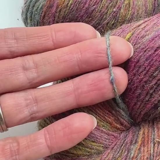 Small-batch dyed heritage skeins of 100% Latvian Dark-Headed Sheep Wool in earthy multicolor gradients like Green-Brown #052. The image shows the rustic single-ply texture and the sheep breed origin, representing the authentic wool traditions of Paces Vilnas Fabrika, Latvia. Available at iDOKNiT.com.