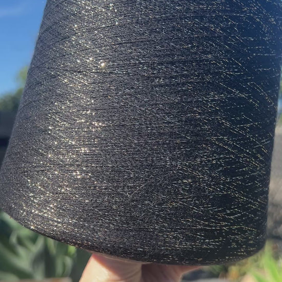 A luxurious cone of Pecci Filati SHIMMER yarn, a modern 50% Cotton, 25% Linen, 14% Polyester, and 12% Polyamide (Lurex) blend. The image showcases the refined metallic glow and delicate texture of this 3400m/100g Italian extrafine yarn, ideal for high-end blending. Authentic luxury fiber available at iDOKNiT.com.