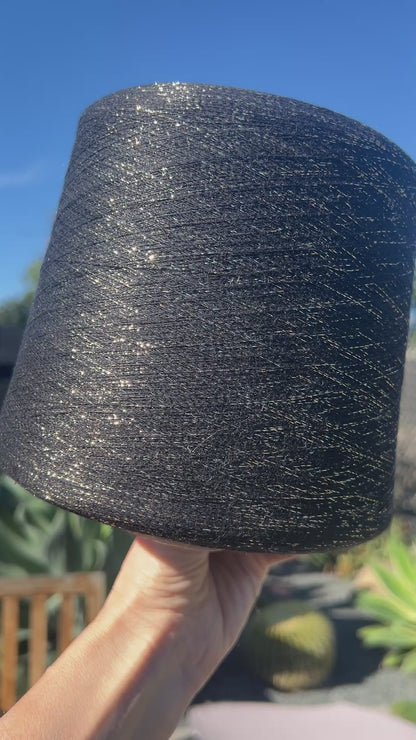A luxurious cone of Pecci Filati SHIMMER yarn, a modern 50% Cotton, 25% Linen, 14% Polyester, and 12% Polyamide (Lurex) blend. The image showcases the refined metallic glow and delicate texture of this 3400m/100g Italian extrafine yarn, ideal for high-end blending. Authentic luxury fiber available at iDOKNiT.com.